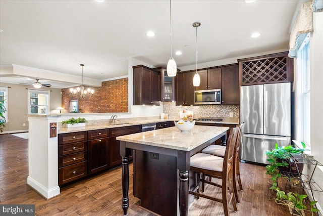 kitchen with a breakfast bar, hanging light fixtures, appliances with stainless steel finishes, a center island, and glass insert cabinets