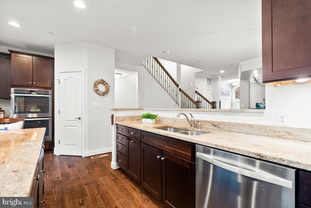 kitchen featuring stainless steel appliances, dark wood finished floors, a sink, and light stone countertops