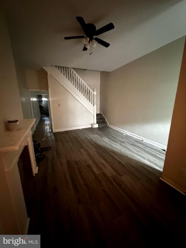 unfurnished living room featuring dark wood-style floors, ceiling fan, baseboards, and stairs