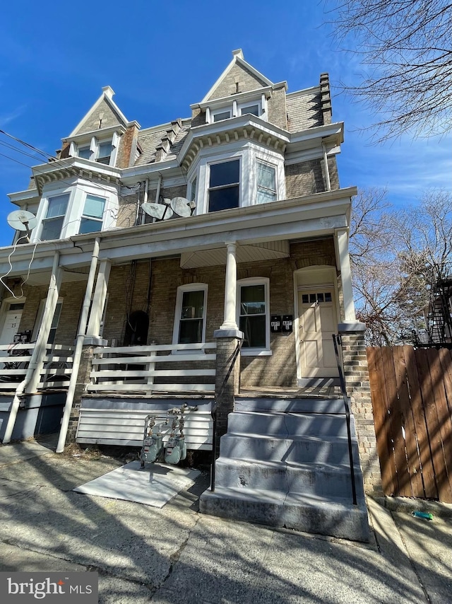 view of front of house featuring a porch, brick siding, fence, and mansard roof