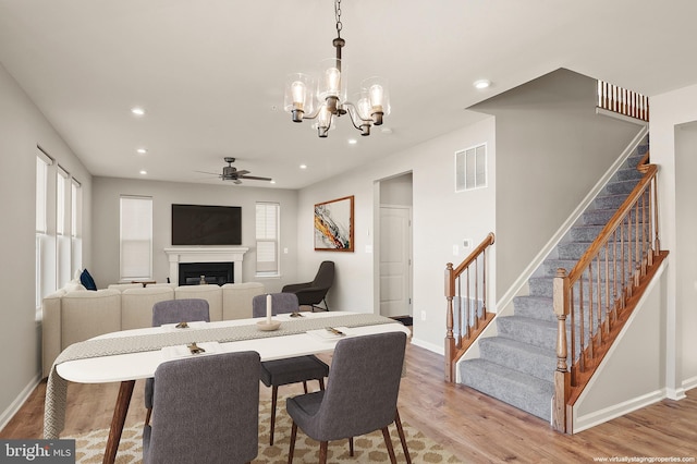 dining space with light wood-style flooring, a glass covered fireplace, visible vents, and stairway