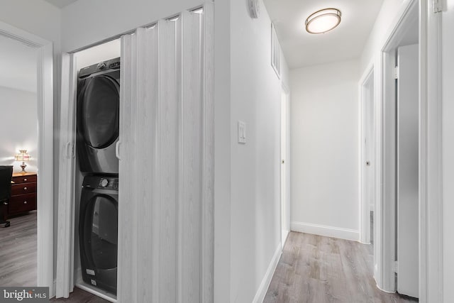 laundry area with stacked washer and dryer, laundry area, light wood-style flooring, and baseboards