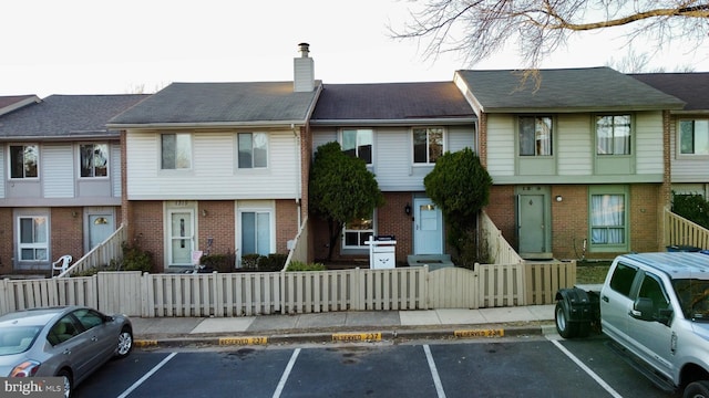 view of front of property featuring uncovered parking, brick siding, a chimney, and a fenced front yard