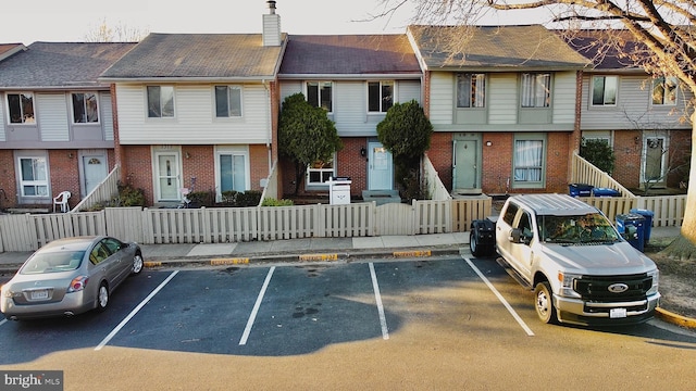 exterior space featuring uncovered parking, brick siding, a chimney, and a fenced front yard