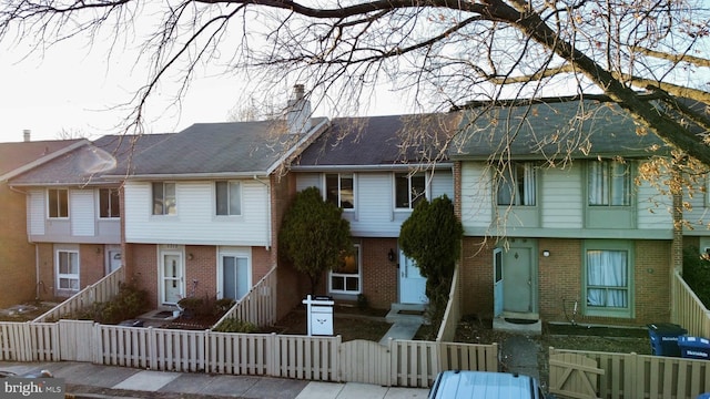 view of property featuring brick siding, a fenced front yard, a chimney, and a gate