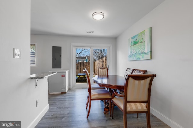 dining room featuring baseboards, electric panel, visible vents, and wood finished floors