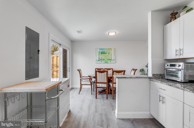 kitchen with light wood finished floors, a toaster, electric panel, visible vents, and white cabinets