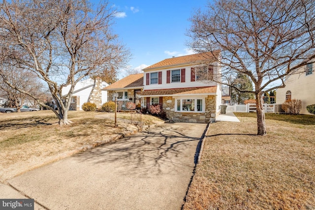 view of front of home featuring a front yard, stone siding, fence, and driveway