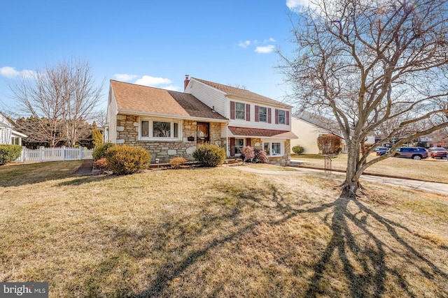 tri-level home with stone siding, a chimney, fence, and a front lawn