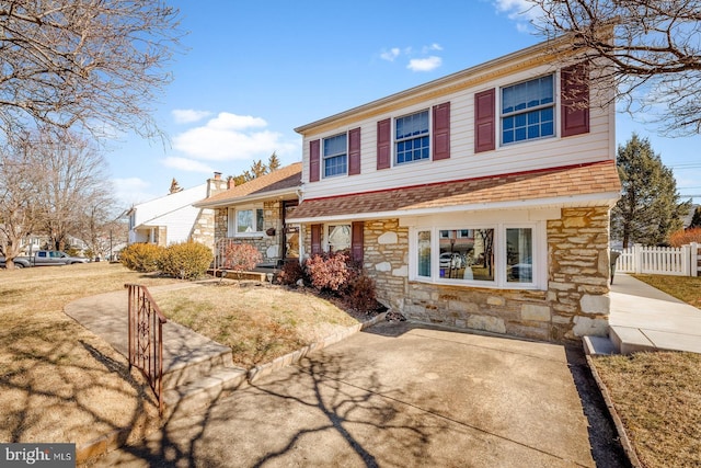 view of front of house featuring stone siding, a chimney, fence, and a front yard