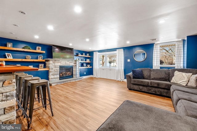 living room featuring recessed lighting, visible vents, a stone fireplace, and wood finished floors