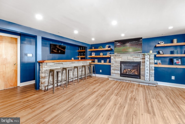 bar with a stone fireplace, a bar, wood finished floors, and recessed lighting