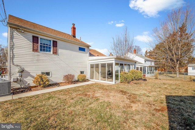 rear view of house with a lawn, a sunroom, a chimney, fence, and central AC