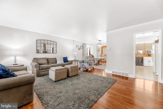 living room featuring baseboards, light wood finished floors, visible vents, and crown molding