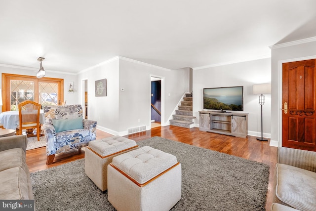 living room featuring stairway, visible vents, wood finished floors, and ornamental molding