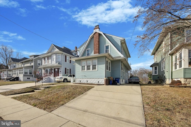 view of front of house featuring a residential view, driveway, a chimney, and a gambrel roof