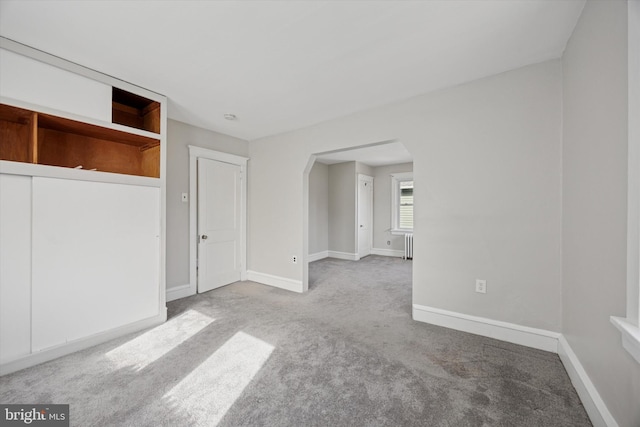 carpeted spare room with arched walkways, radiator heating unit, and baseboards