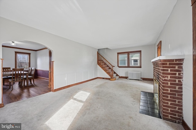 carpeted living room with arched walkways, radiator, a wainscoted wall, and a healthy amount of sunlight