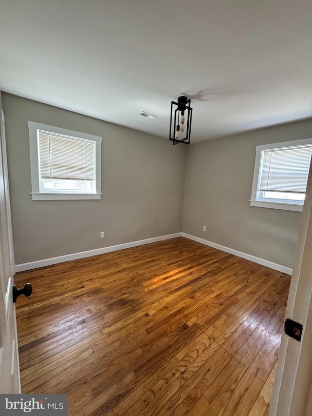 spare room with wood-type flooring, visible vents, and baseboards