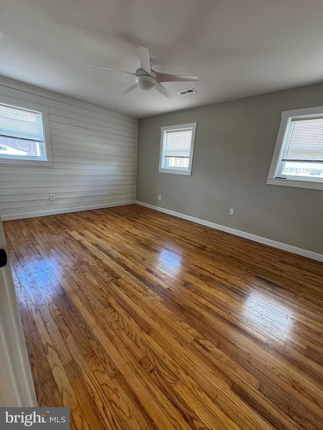 unfurnished room with hardwood / wood-style floors, a ceiling fan, visible vents, and baseboards