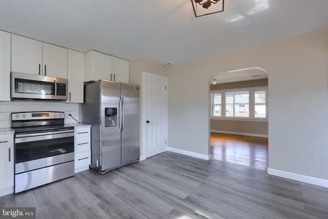 kitchen with arched walkways, light wood-style flooring, stainless steel appliances, white cabinets, and light countertops