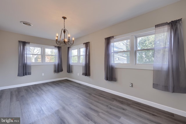 spare room with a notable chandelier, dark wood finished floors, visible vents, and baseboards