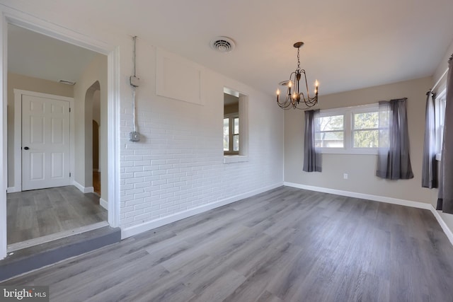 unfurnished dining area featuring a chandelier, arched walkways, brick wall, wood finished floors, and visible vents