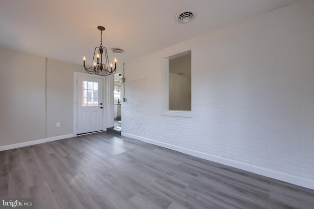 foyer featuring an inviting chandelier, brick wall, visible vents, and wood finished floors