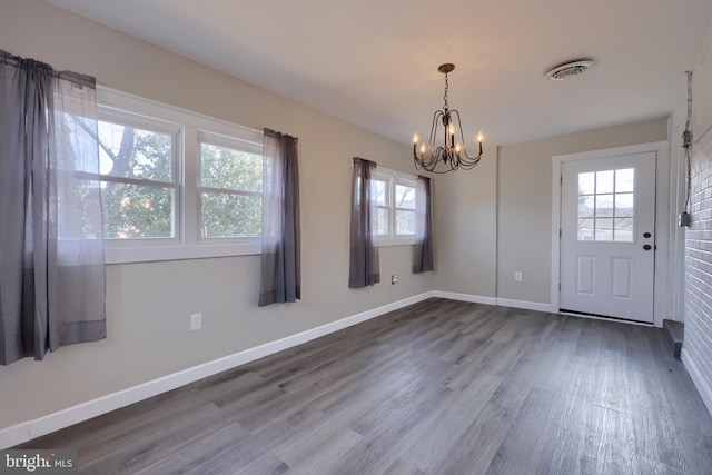 unfurnished dining area with an inviting chandelier, wood finished floors, visible vents, and baseboards