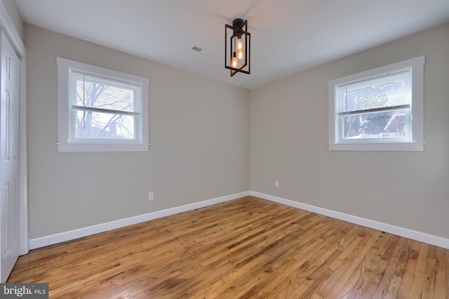 spare room with light wood finished floors, visible vents, and baseboards