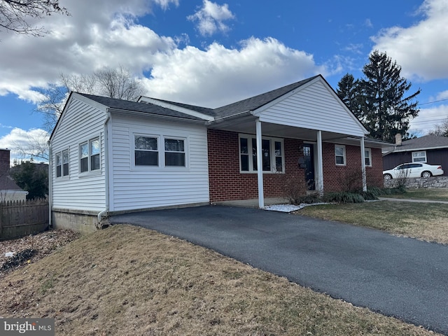 view of front of house featuring driveway, brick siding, fence, and a front yard