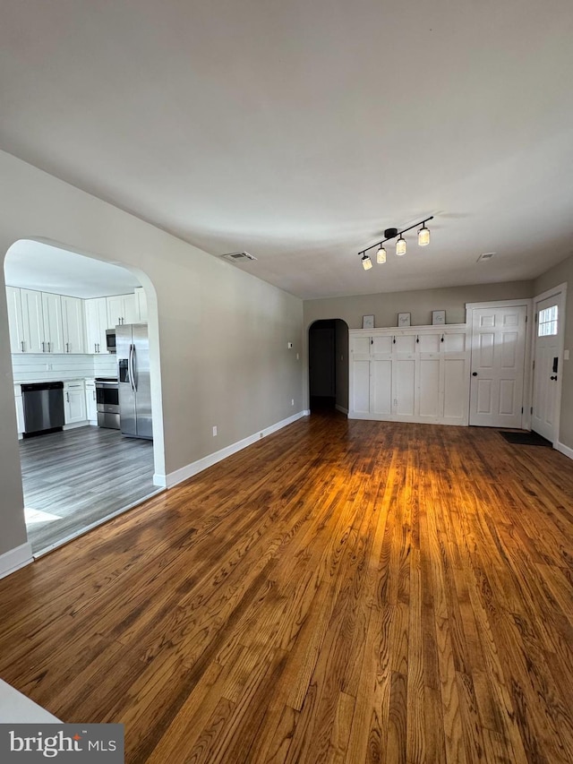 unfurnished living room with baseboards, visible vents, arched walkways, and dark wood-type flooring