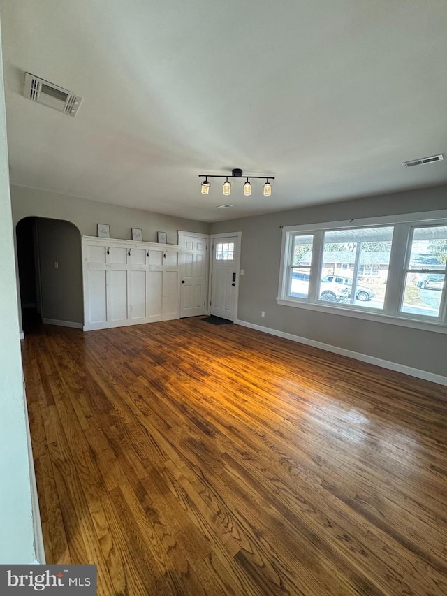 unfurnished room featuring dark wood-style floors, baseboards, visible vents, and arched walkways