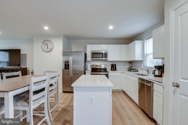 kitchen featuring light wood-style flooring, stainless steel appliances, a sink, a center island, and tasteful backsplash