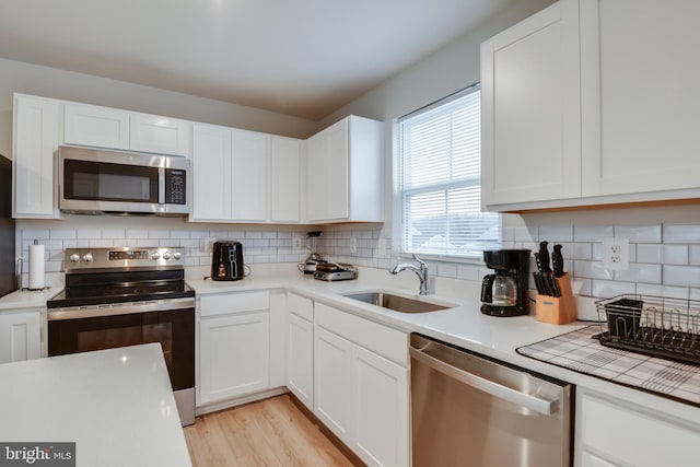 kitchen with stainless steel appliances, tasteful backsplash, a sink, and white cabinetry