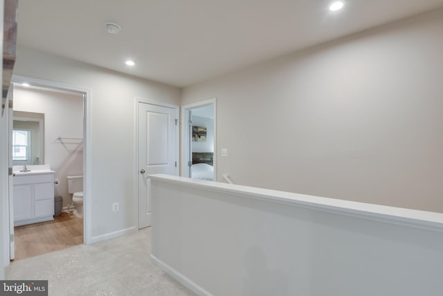 hall featuring baseboards, a sink, and recessed lighting