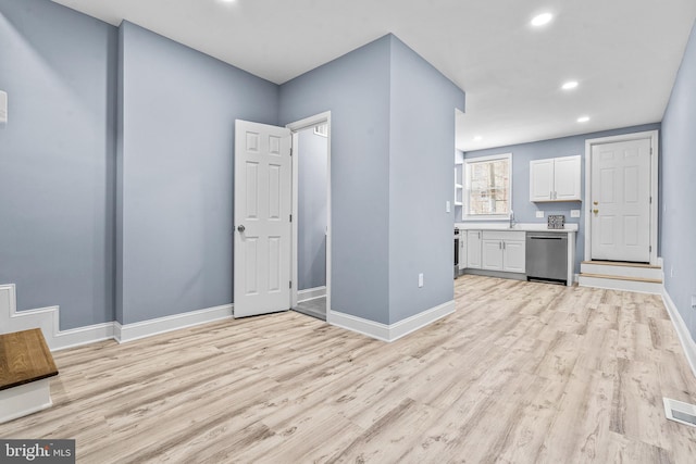 interior space with light wood-style flooring, baseboards, white cabinets, light countertops, and dishwasher