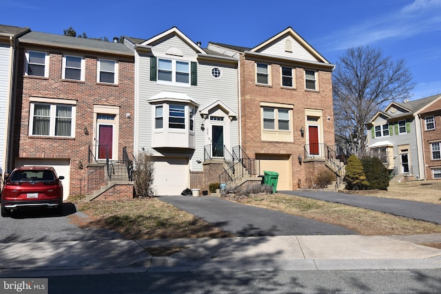 view of property featuring brick siding, an attached garage, a residential view, and aphalt driveway