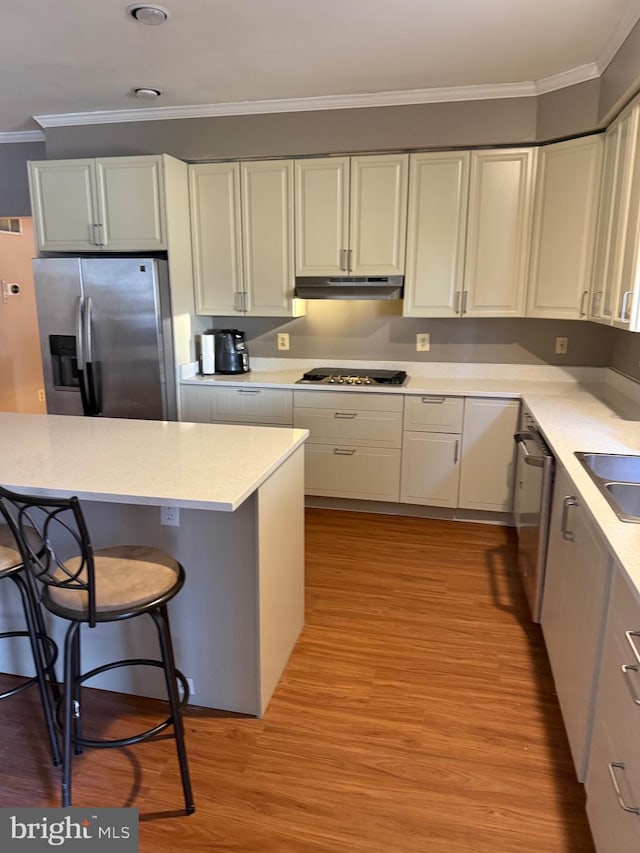 kitchen with light wood-type flooring, under cabinet range hood, appliances with stainless steel finishes, white cabinets, and crown molding