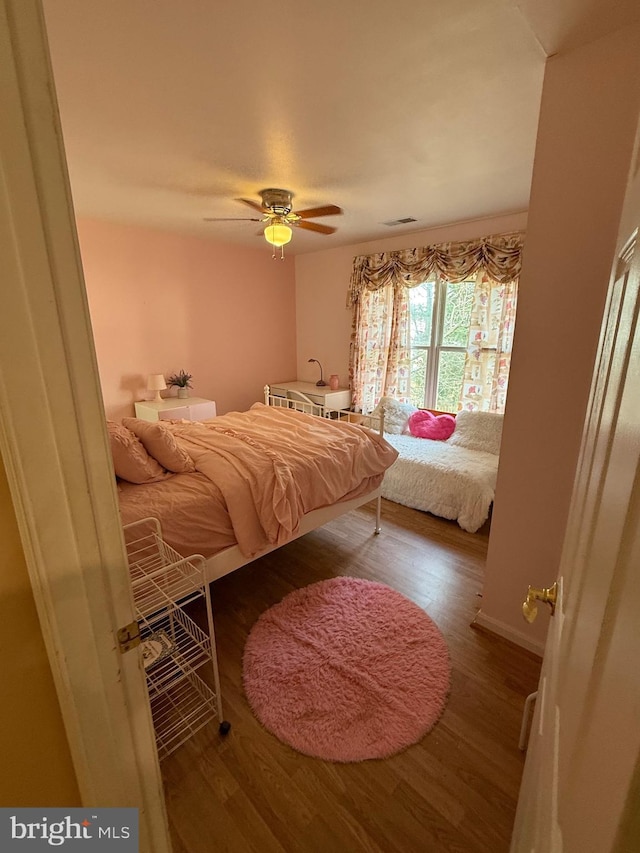 bedroom with a ceiling fan, wood finished floors, visible vents, and baseboards