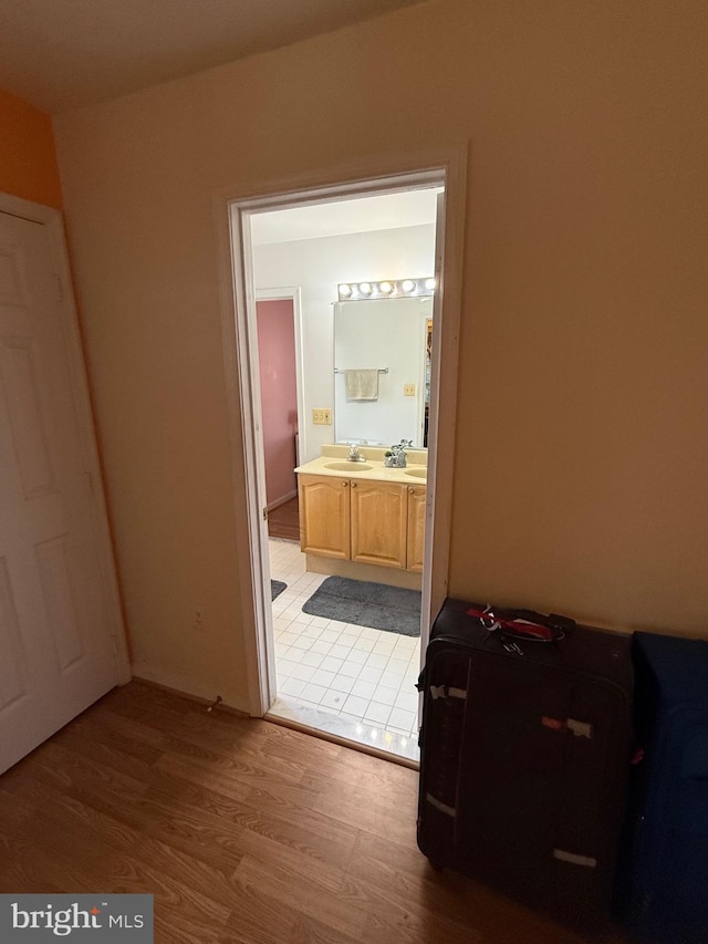 bedroom with connected bathroom, light wood finished floors, and a sink