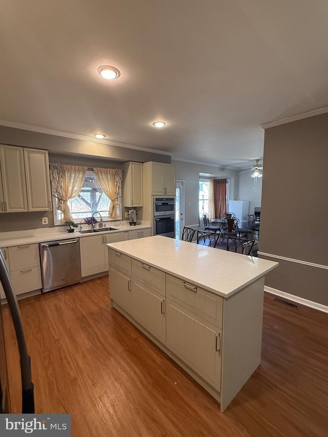 kitchen with wood finished floors, a sink, light countertops, appliances with stainless steel finishes, and crown molding