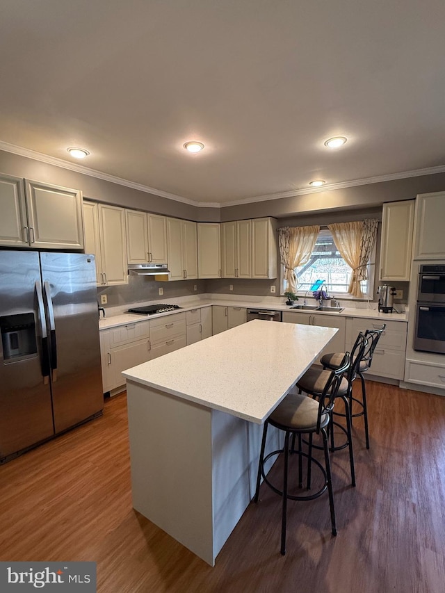 kitchen with a kitchen bar, dark wood-type flooring, a kitchen island, appliances with stainless steel finishes, and light countertops