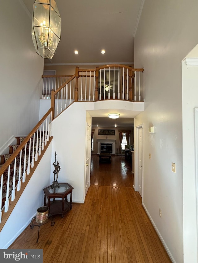 interior space featuring stairway, baseboards, hardwood / wood-style flooring, a glass covered fireplace, and crown molding