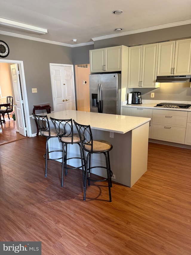 kitchen with dark wood-type flooring, under cabinet range hood, light countertops, ornamental molding, and stainless steel appliances