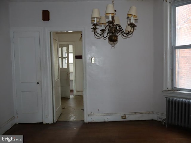 unfurnished dining area featuring a chandelier, plenty of natural light, radiator heating unit, and wood finished floors