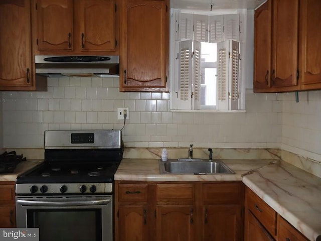 kitchen featuring under cabinet range hood, a sink, light countertops, brown cabinetry, and gas range