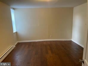 spare room with a baseboard heating unit, baseboards, and dark wood-style floors