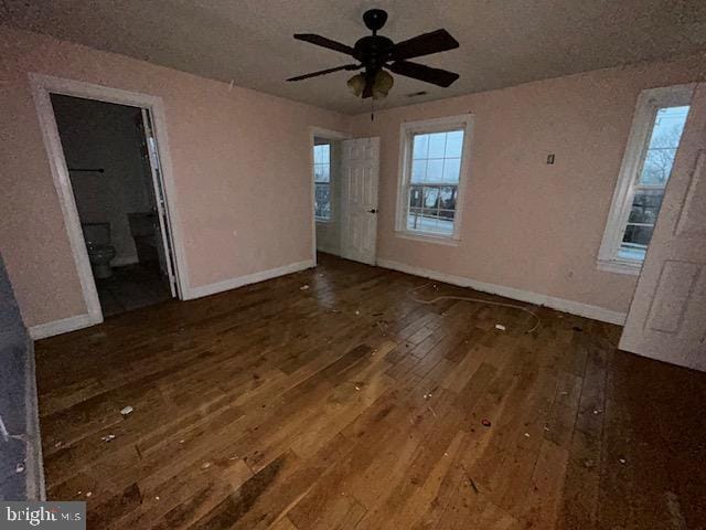 unfurnished bedroom with connected bathroom, baseboards, and hardwood / wood-style floors