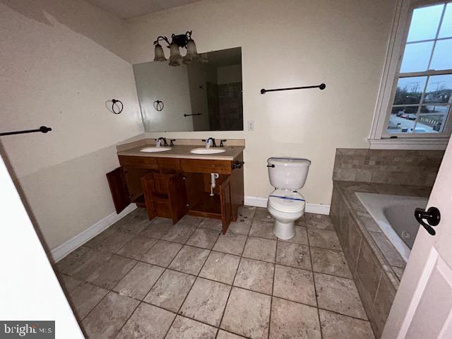 bathroom featuring toilet, tiled bath, double vanity, and a sink